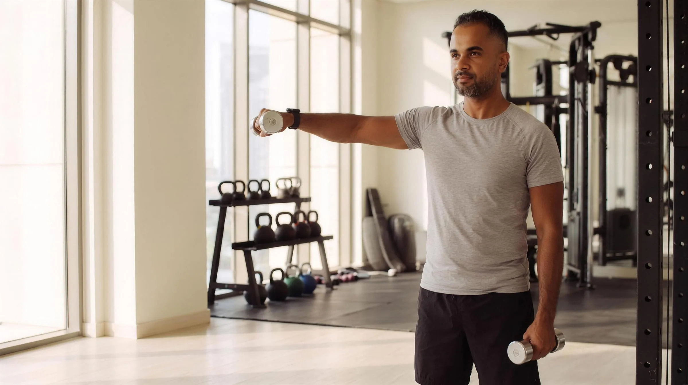 A man lifting light dumbbells in a sunlit gym